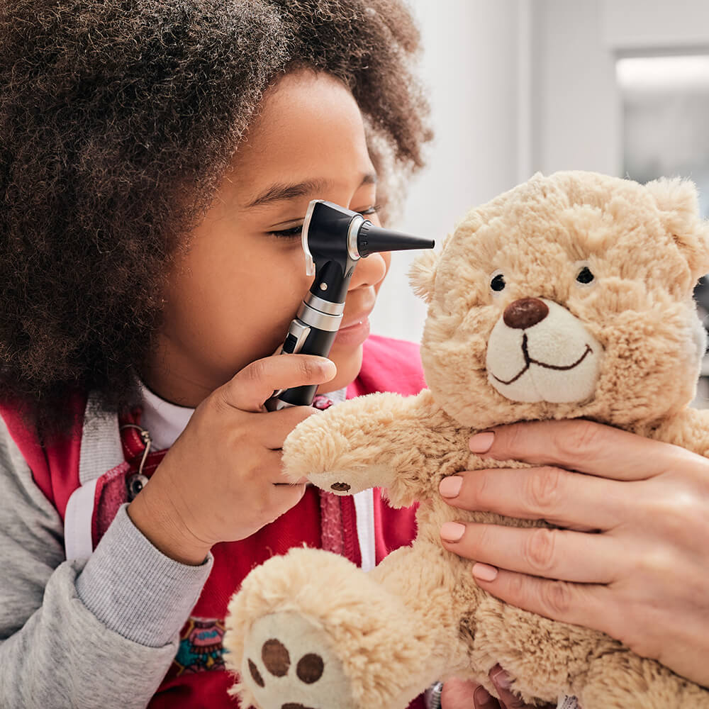 girl playing as audiologist looking at teddy bear ear